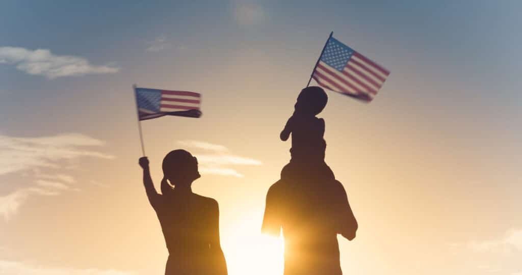 A family in silhouette waving American flags